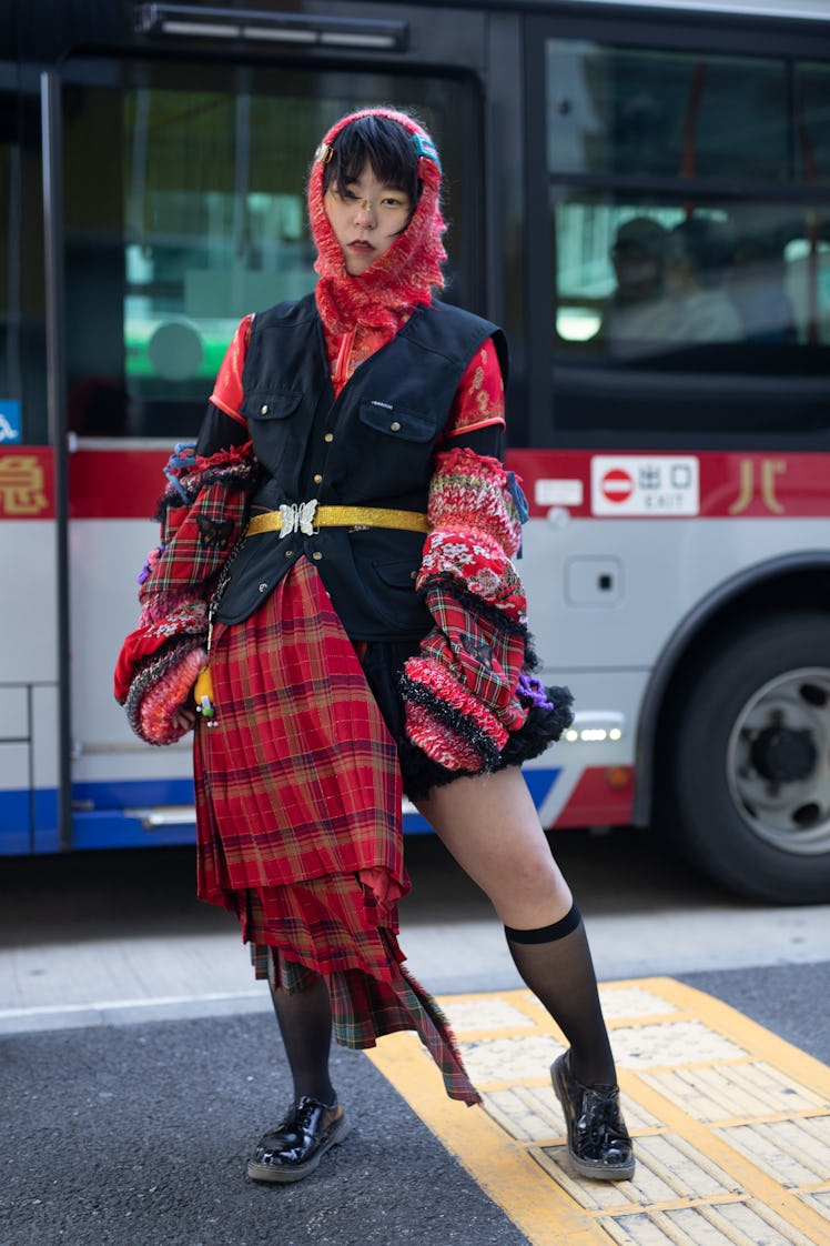 A guest is seen wearing black utility vest, red plaid skirt, red knit hood, red top and red knit arm...