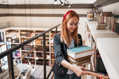 Young beautiful redhead female student reading books and learning in a college library.