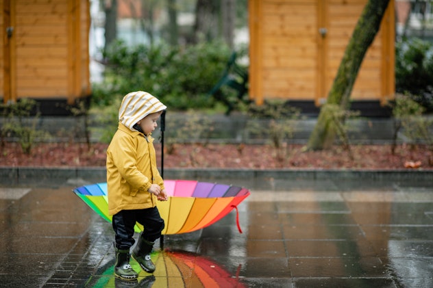 Child playing with colorful umbrella, jumping in puddles and playing in the rain