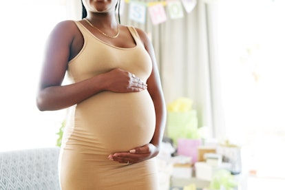 A pregnant person standing up with their hands cradling their belly.