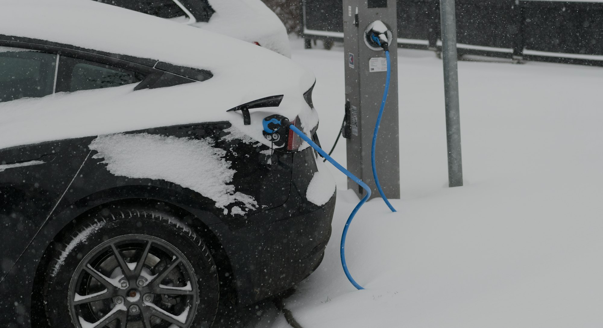 Electric cars charging at an electric vehicle charging station during a cold winter day with fresh s...