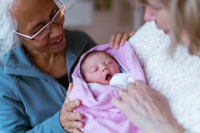 A beautiful moment that shows a mixed race asian grandmother and a Caucasian grandmother holding the...