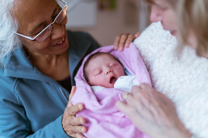 A beautiful moment that shows a mixed race asian grandmother and a Caucasian grandmother holding the...