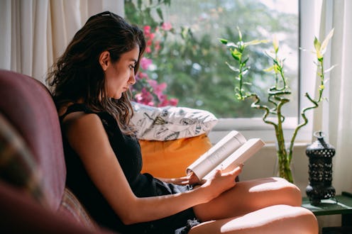 Young Woman Reading a Book by the Window at Home