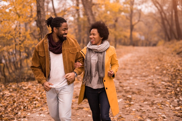 Cheerful African American couple having fun and talking while walking in nature during autumn.