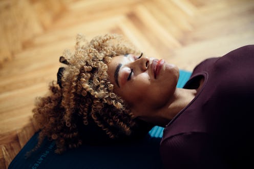 Close-up side view of an Afro-American woman lying on the yoga mat on the floor and smiling. She loo...