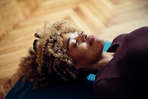 Close-up side view of an Afro-American woman lying on the yoga mat on the floor and smiling. She loo...