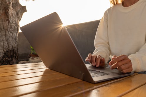 View of woman working on her laptop in a tropical garden.