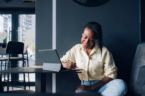 Happy African-American business woman writing notes while discuss with clients or coworkers at onlin...