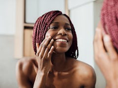 Beautiful  smiling African woman standing in front of a mirror and looking at her face wrinkles.