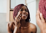 Beautiful  smiling African woman standing in front of a mirror and looking at her face wrinkles.