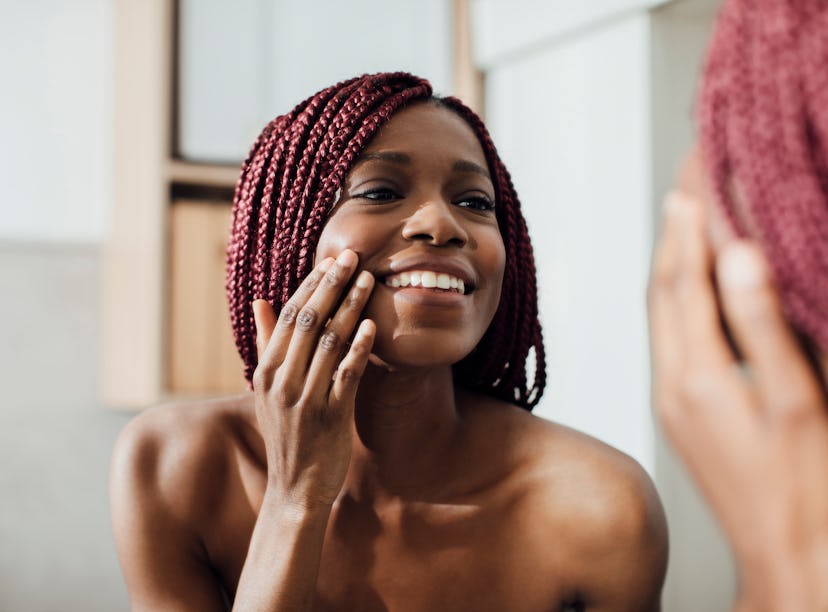 Beautiful  smiling African woman standing in front of a mirror and looking at her face wrinkles.