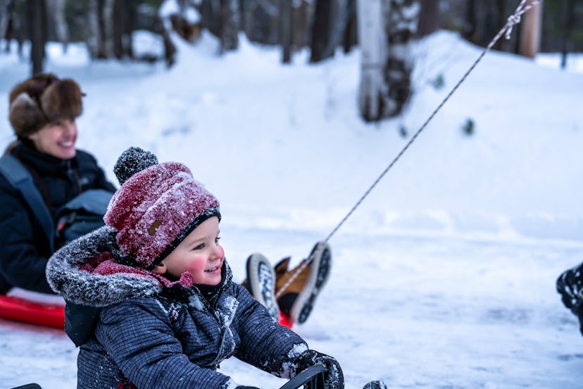 A young boy sitting on his sleigh and being pulled during winter in Quebec.