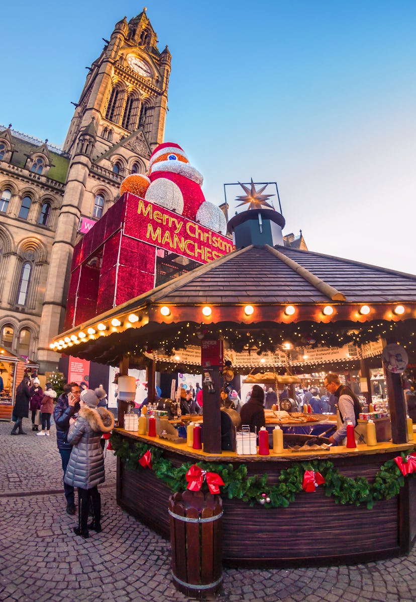 Christmas market placed in Albert square with Manchester Town hall in the background. There is a cou…