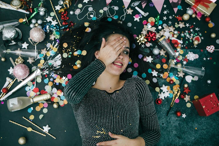 Young woman laying in a pile of confetti on New Year's Eve after reading the December 27, 2021 weekl...