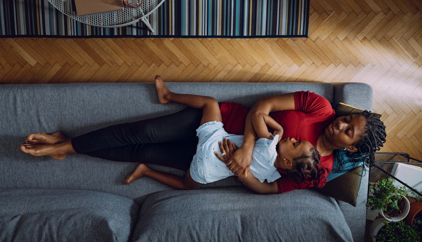 Directly above photo of tired mother with daughter lying down on cozy couch in living room, cuddling...