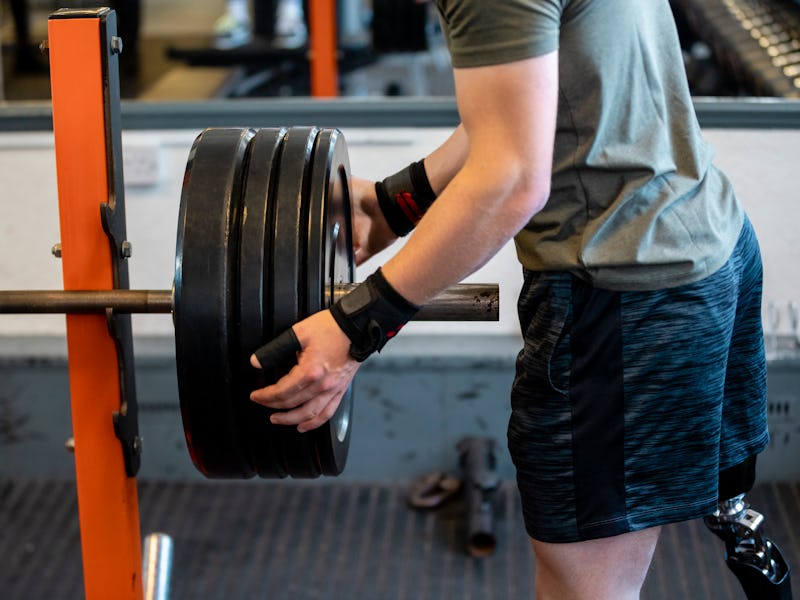 A mid-section shot of an unrecognizable young teenage male athlete putting an extra weight plate on ...
