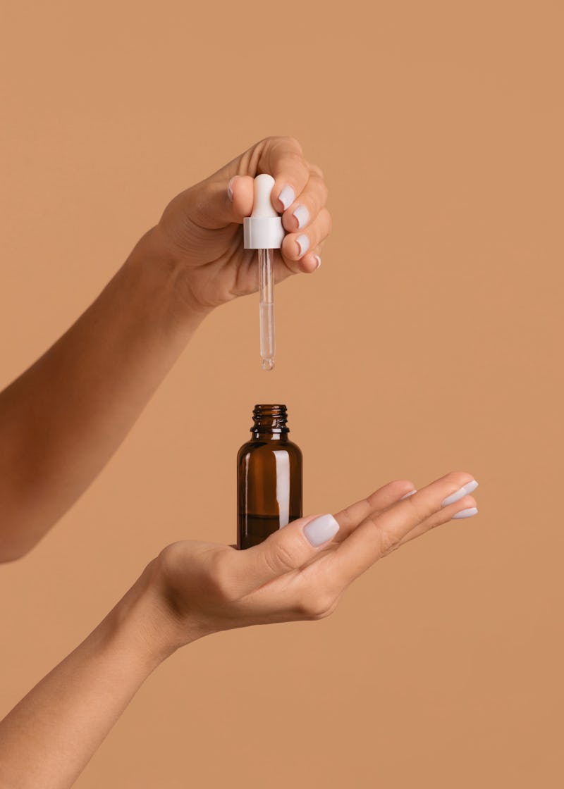 Hands extracting a dark spot serum from its bottle using a pipette 