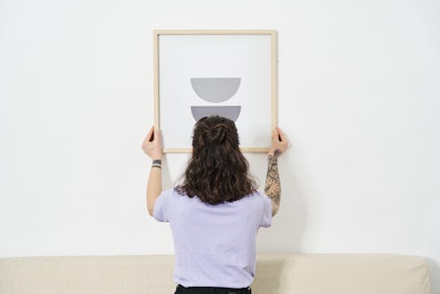 Back view of a woman hanging a picture on the wall at home. Home improvement and decoration concept.