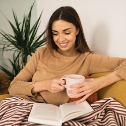 Woman enjoying at home, drinking coffee and reading a book.