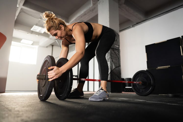 Active and healthy, Caucasian sportswoman, adjusting the weight on the barbell, while exercising in ...