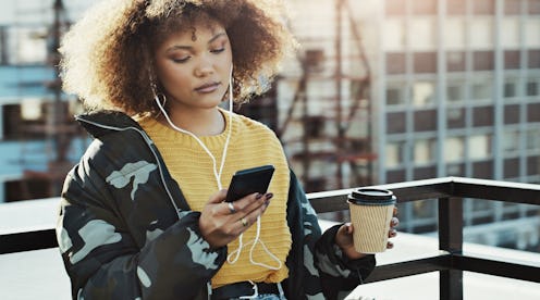 Shot of an attractive young woman using a smartphone to listen to music in the city