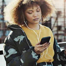 Shot of an attractive young woman using a smartphone to listen to music in the city