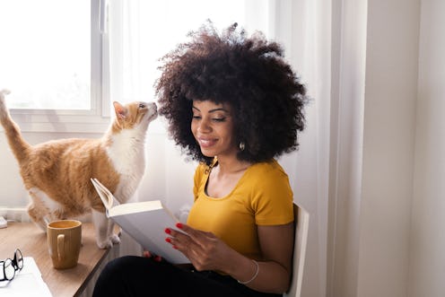 woman reading a book with her cat keeping her company
