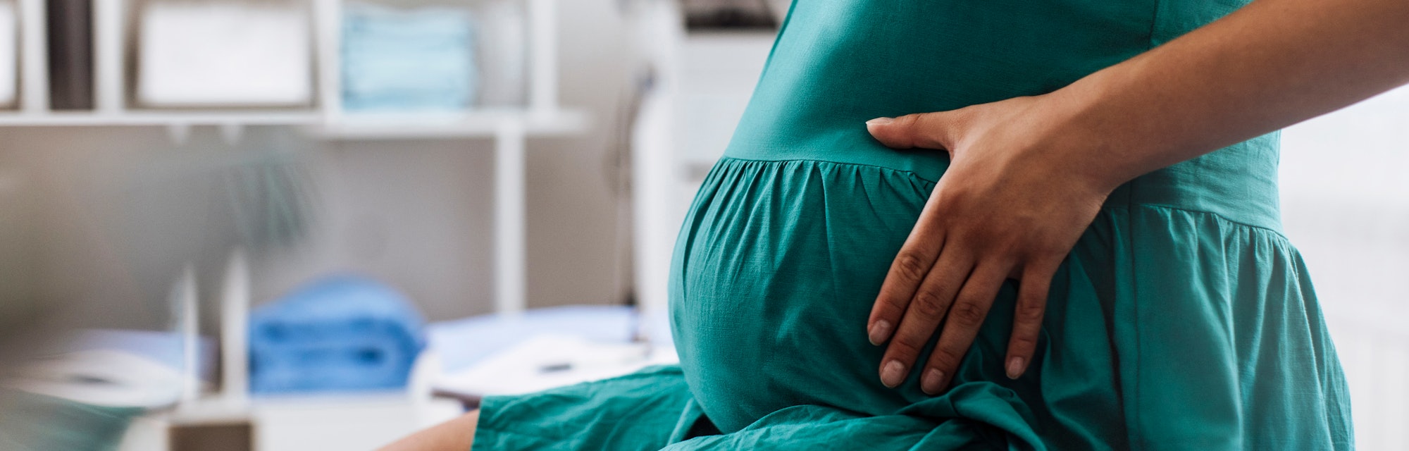 Unrecognisable pregnant woman holding her belly while sitting at the doctors office
