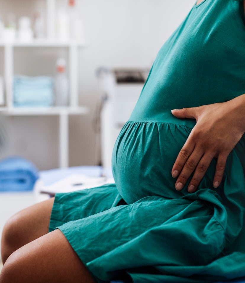 Unrecognisable pregnant woman holding her belly while sitting at the doctors office, in a story abou...