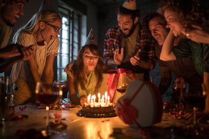 Young woman blowing out candles while having a winter Birthday party with her friends at home.
