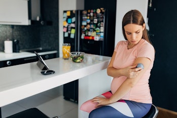 Gorgeous pregnant woman performs a daily blood sugar test while sitting at the bar in the kitchen