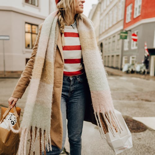 Photo of a young woman carrying paper bags while walking down the street; spending her day outdoors ...
