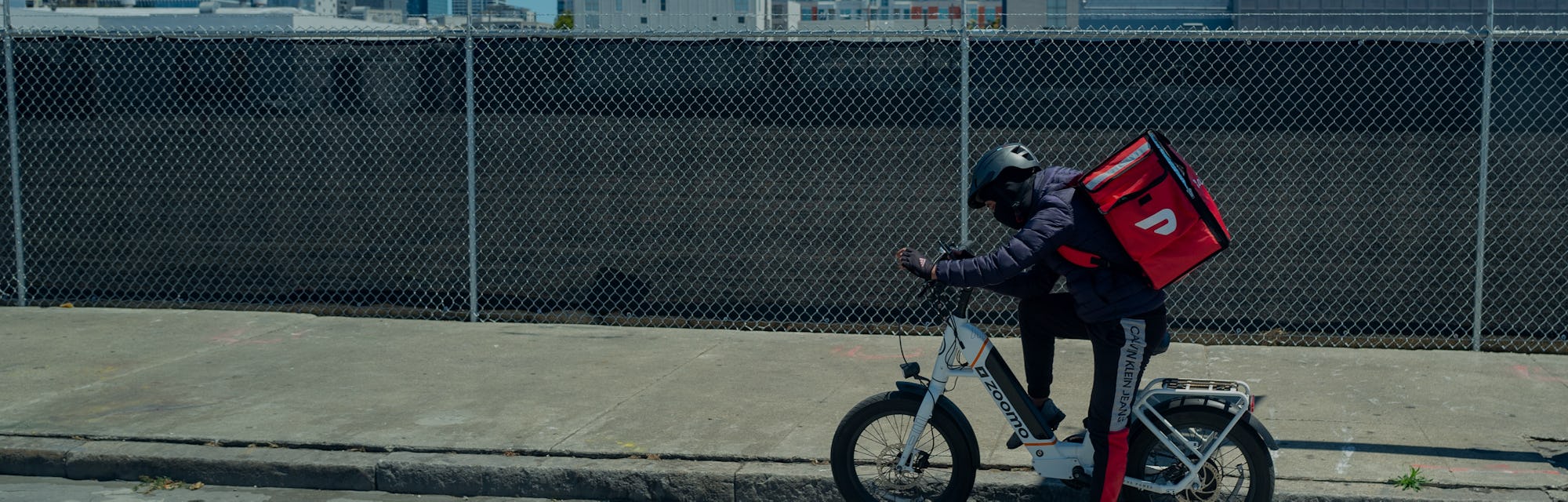 Doordash driver on electric bicycle wearing a cooler backpack and consulting phone with skyline of S...