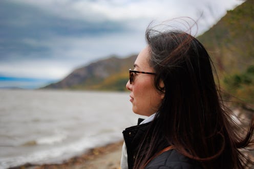 Side view of woman standing on shore and looking ahead. Windy autumn weather. Asian mid adult female...