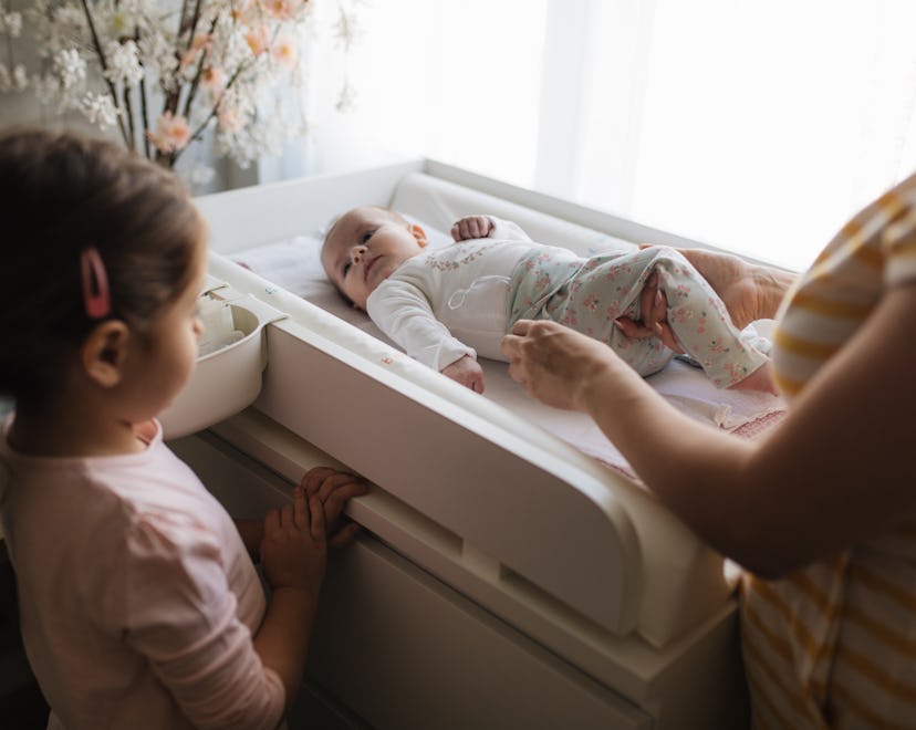 Little girl watching her mom change clothes of her little baby sister