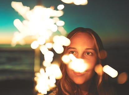 Young woman holding a sparkler on the beach, thinking about how her zodiac sign will have the worst ...