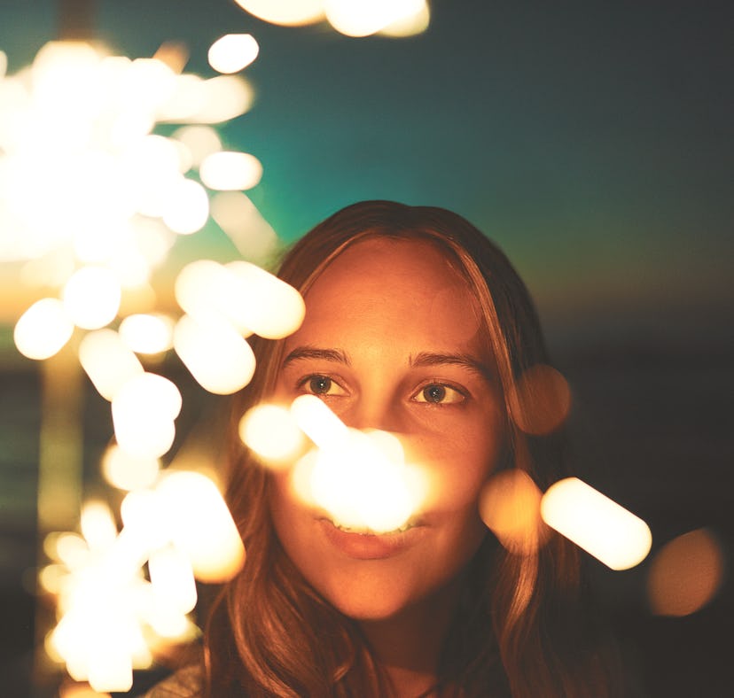Young woman holding a sparkler on the beach, thinking about how her zodiac sign will have the worst ...