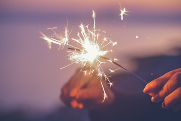 Two young people holding sparklers on the beach, thinking about how their zodiac signs will have the...