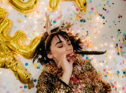 Young woman lying down on the floor, surrounded by confetti, thinking about how her zodiac sign will...