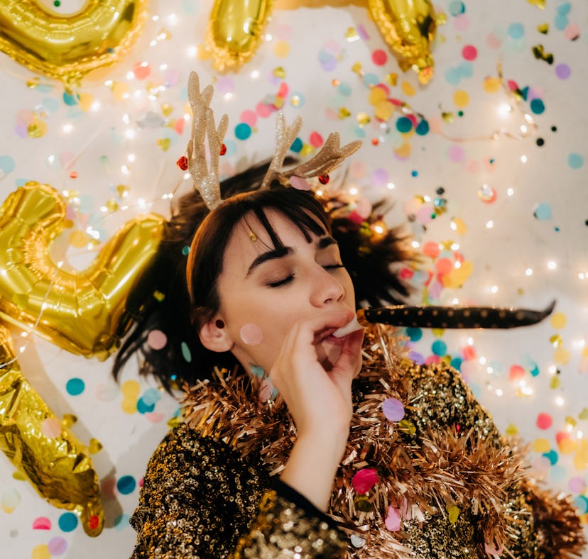 Young woman lying down on the floor, surrounded by confetti, thinking about how her zodiac sign will...