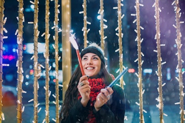 Young woman holding sparklers in winter, thinking about how her zodiac sign will have the best New Y...