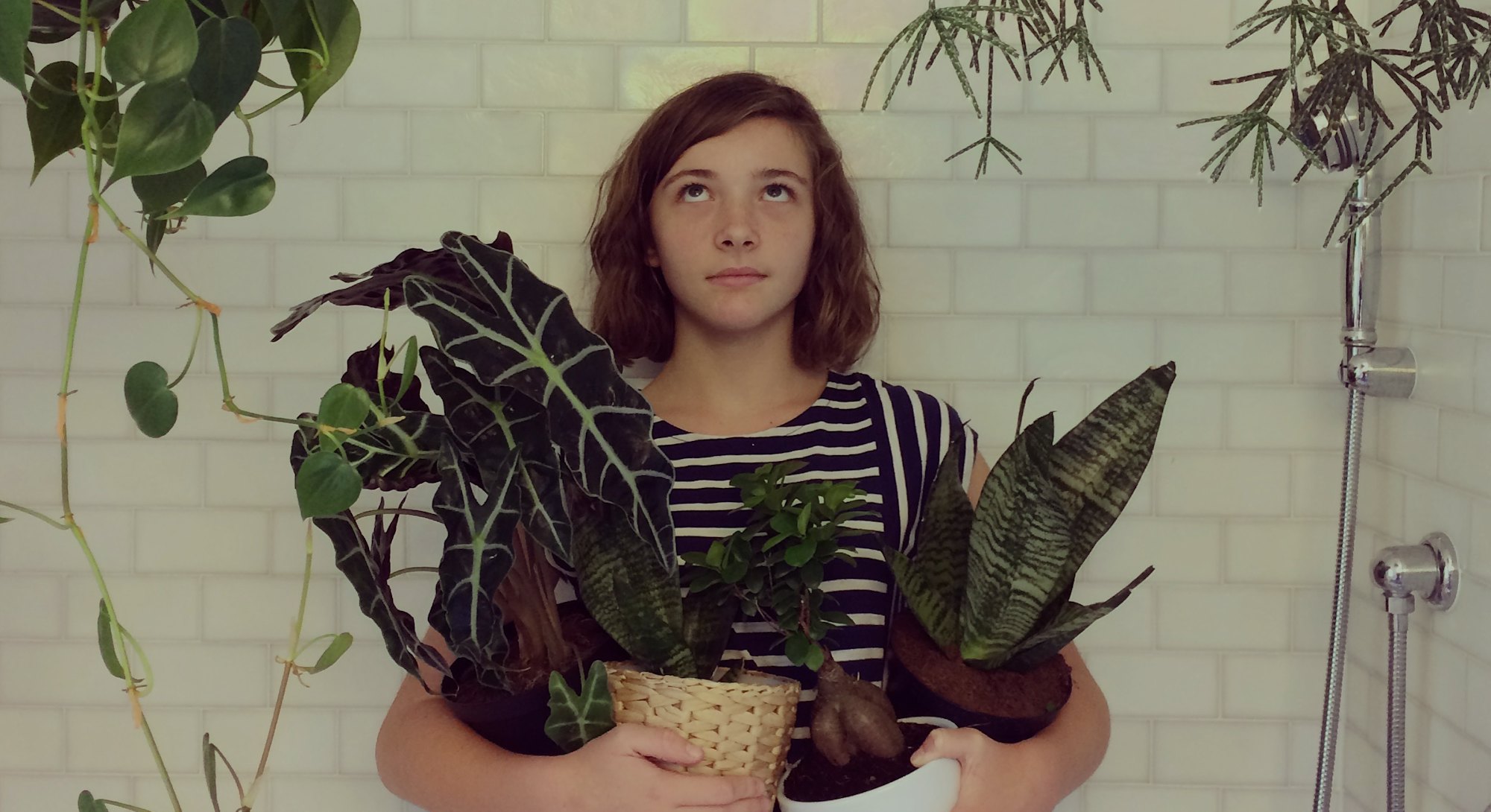 Portrait of a young girl with a funny expression holding potted plants and surrounded by a jungle of...