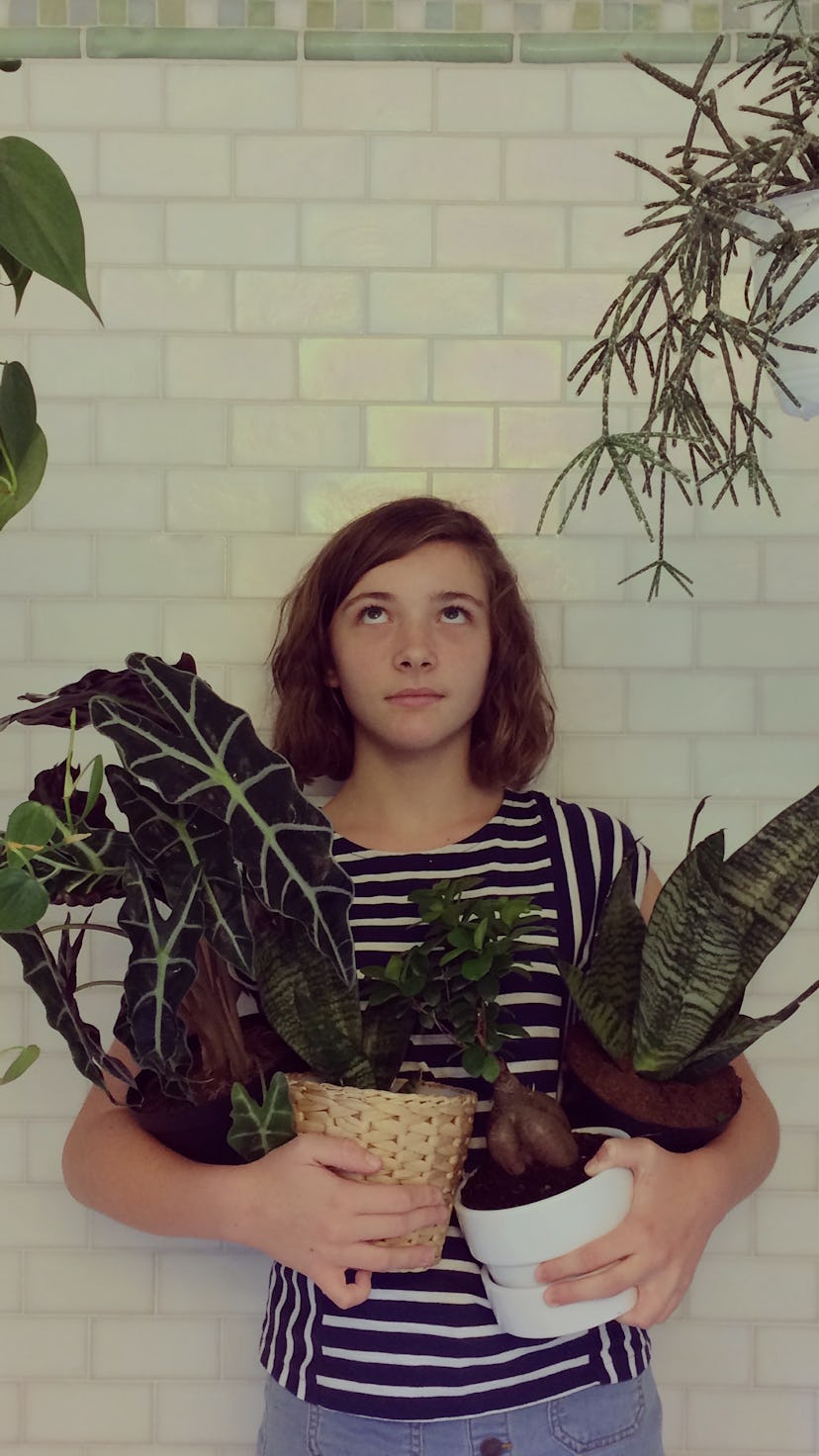 Portrait of a young girl with a funny expression holding potted plants and surrounded by a jungle of...