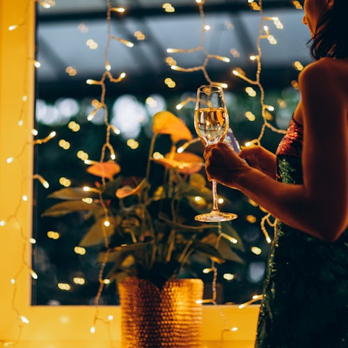 Woman in a festive dress with a glass of champagne in her hand against the background of Christmas l...