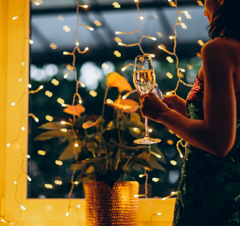 Woman in a festive dress with a glass of champagne in her hand against the background of Christmas l...