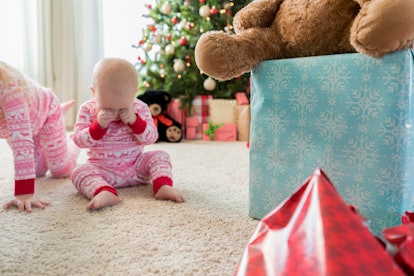 Adorable baby girl rubs her eyes while waiting to open presents on Christmas morning. Her sister is ...