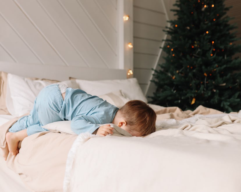 A sad moody little child boy in cozy pajamas is sad and crying lying on the bed closing his eyes in ...