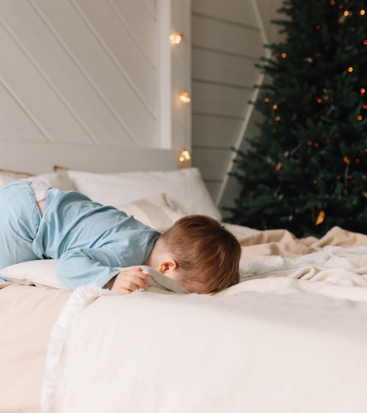 A sad moody little child boy in cozy pajamas is sad and crying lying on the bed closing his eyes in ...