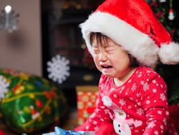A girl crying while wearing red holiday pajamas and a red Santa cap